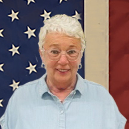 Sharon smiling in front of an american flag with a blue shirt and white glasses